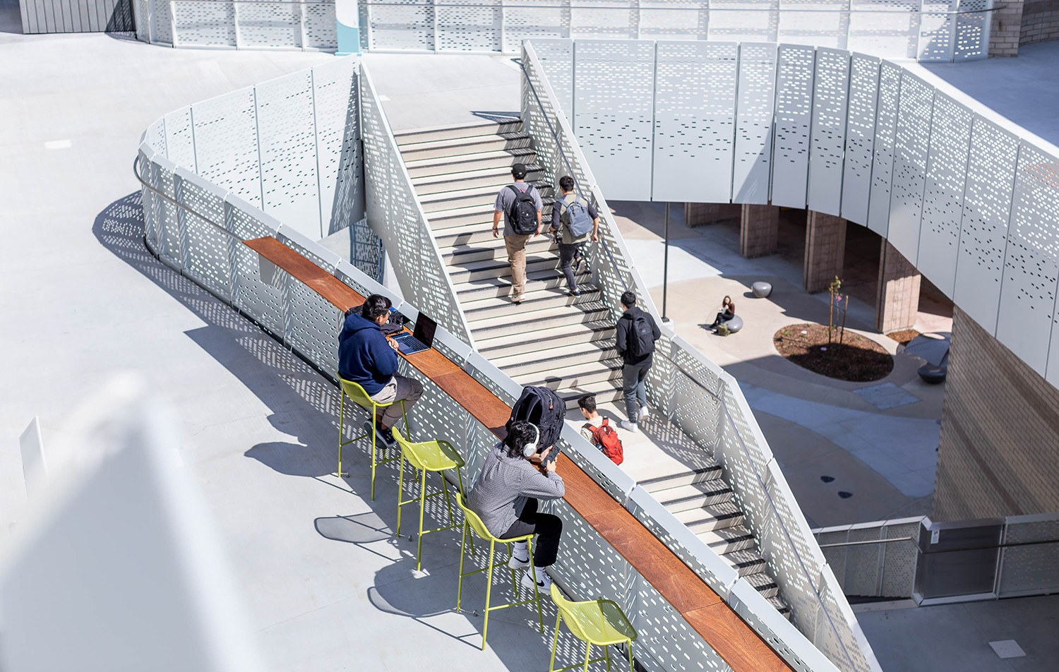 photo looking down from a third story balcony showing two seated students at a rail on the second story with more climbing stairs